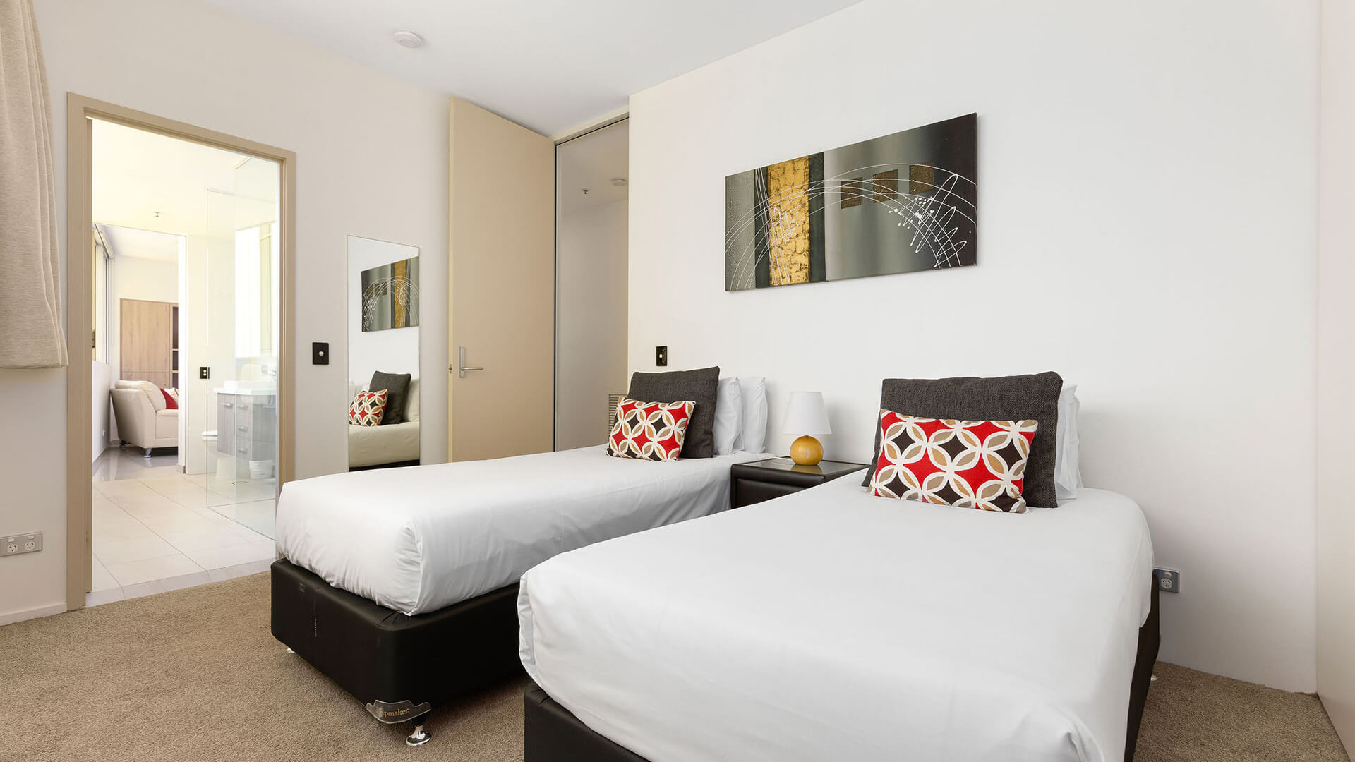 Twin bedroom with white linens, geometric cushions, and abstract wall art in ULTIQA Air’s 3 Bedroom Ocean View Suite.