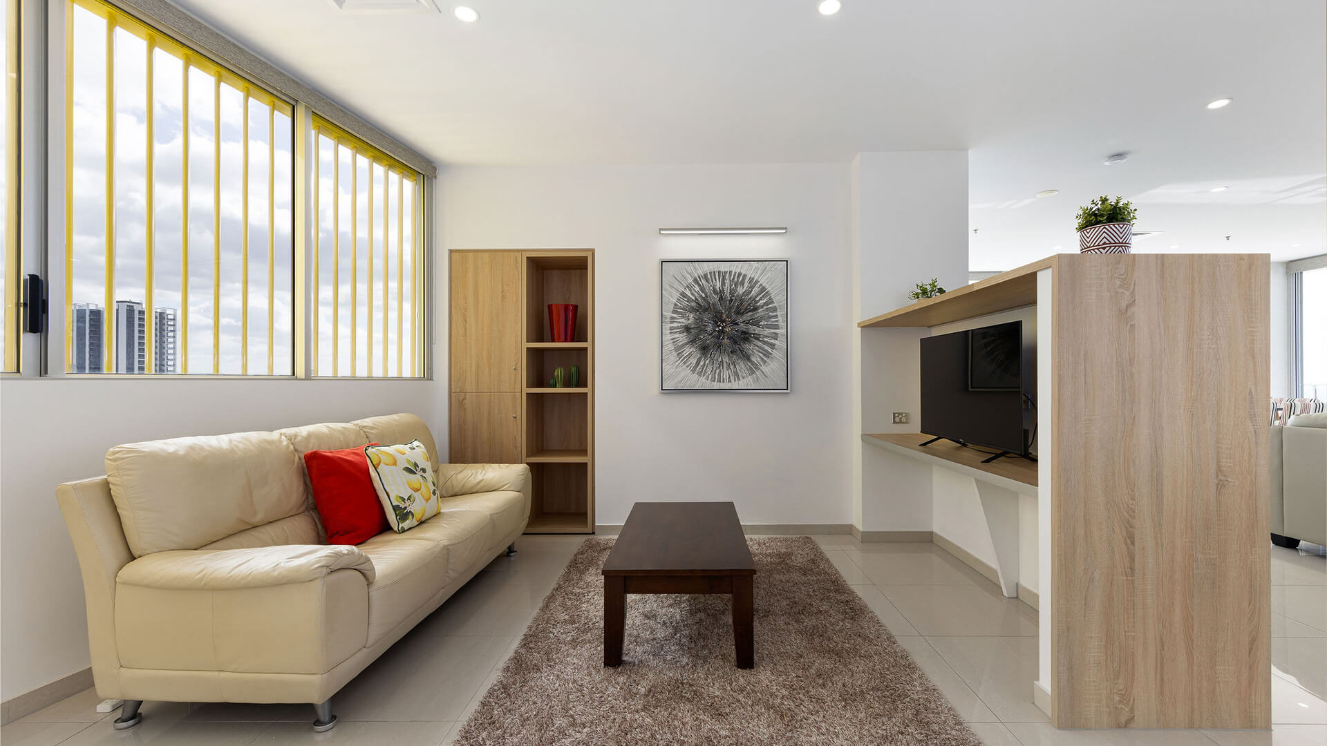 Media room with beige sofa, wood coffee table, and vertical blinds in ULTIQA Air’s 3 Bedroom Ocean View Suite.