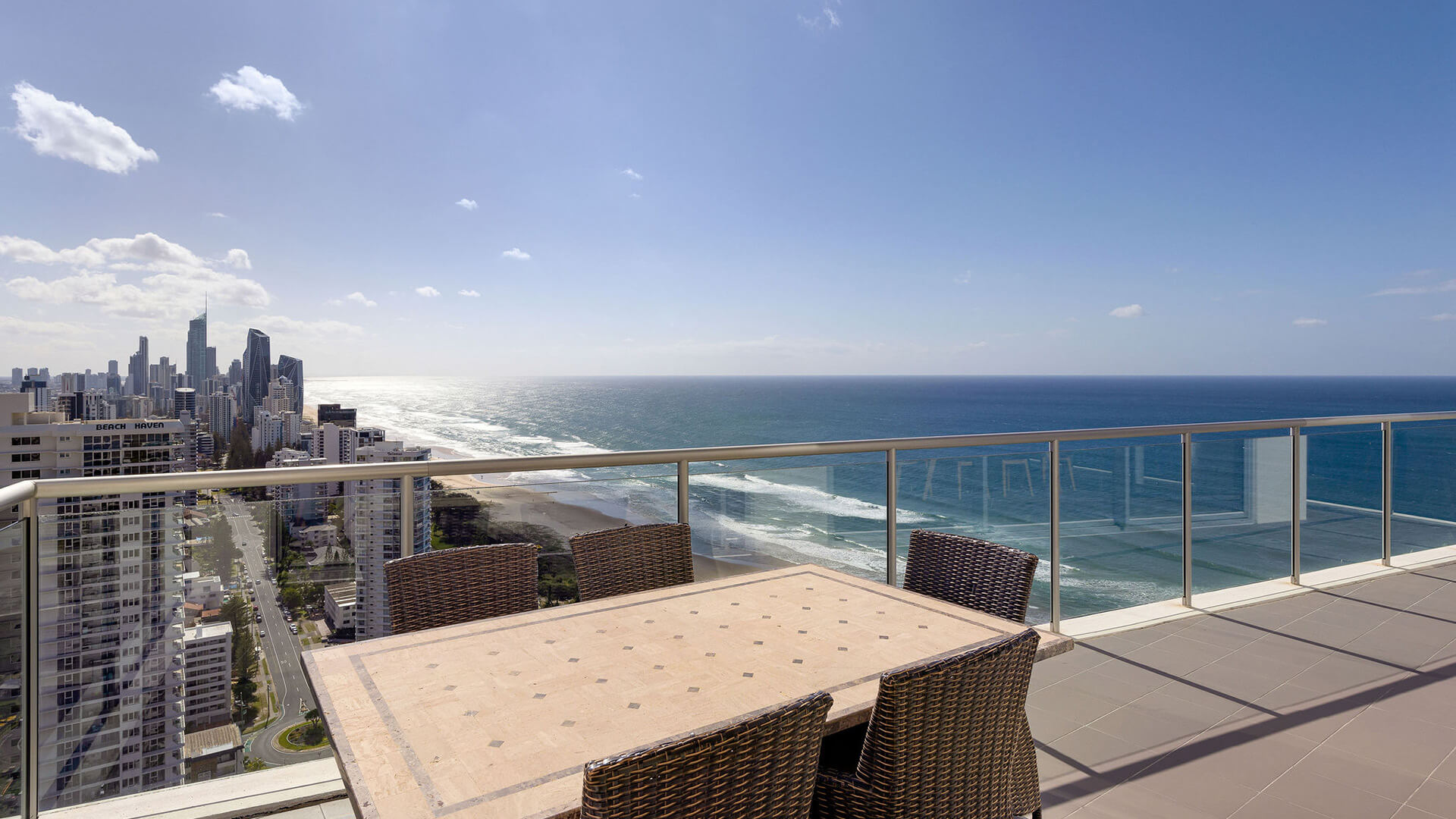 Balcony with wicker chairs and table overlooking Gold Coast skyline and ocean.