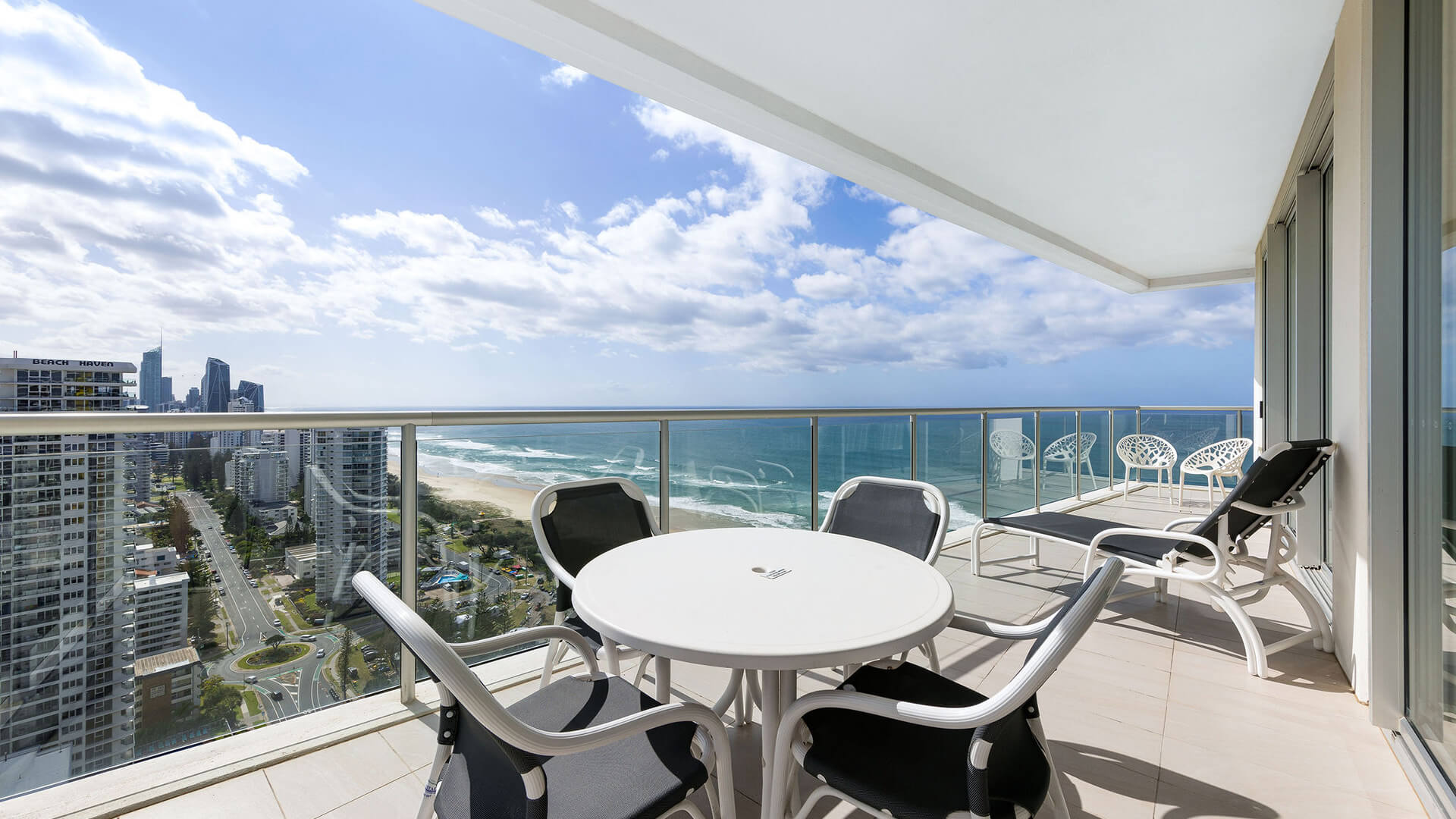 Balcony with round table, lounge chair, and ocean views in ULTIQA Air’s 3 Bedroom Ocean View Suite.