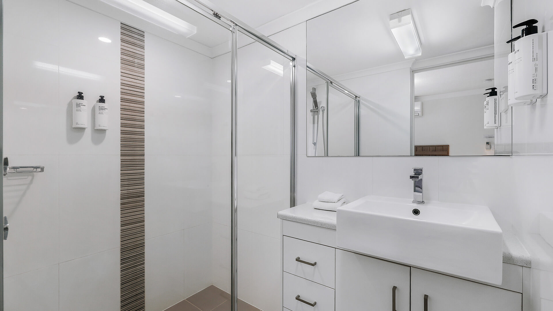 Modern bathroom at ULTIQA Beach Haven featuring a walk-in shower, large vanity, and mirrored cabinetry with complimentary amenities.