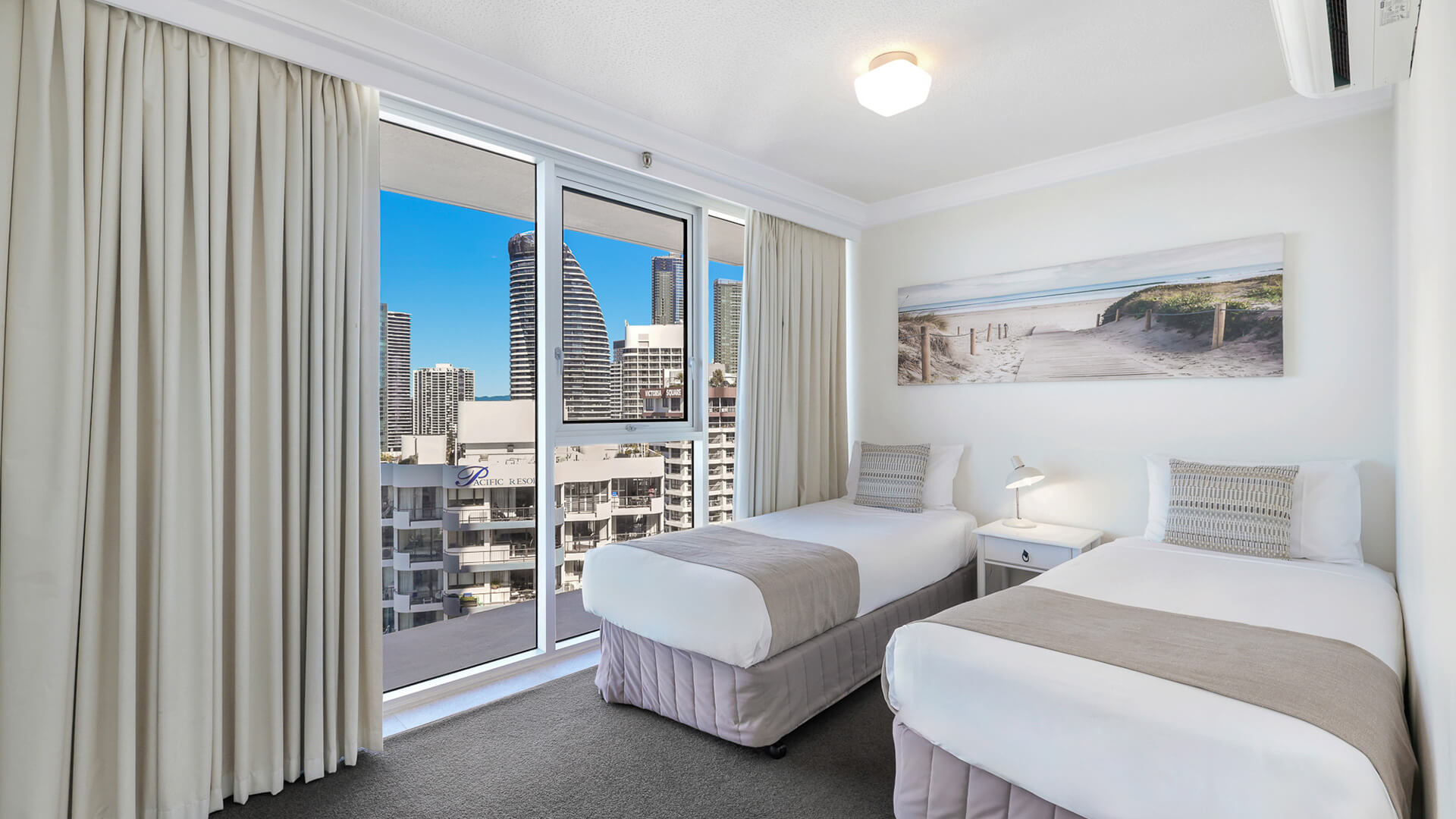 Twin bedroom at ULTIQA Beach Haven featuring city views, coastal artwork, air conditioning, and natural light.