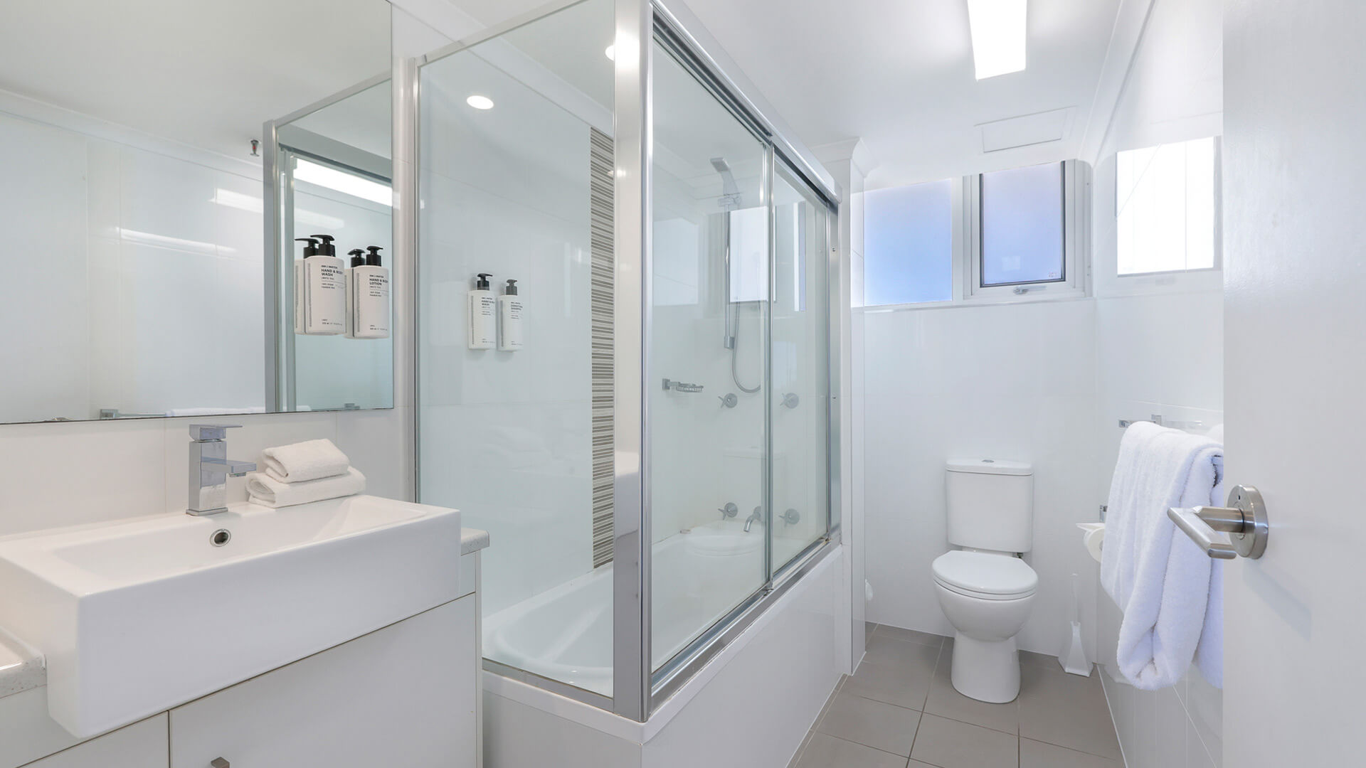 Bright bathroom at ULTIQA Beach Haven featuring a shower-over-bath, modern vanity, toilet, and complimentary amenities.