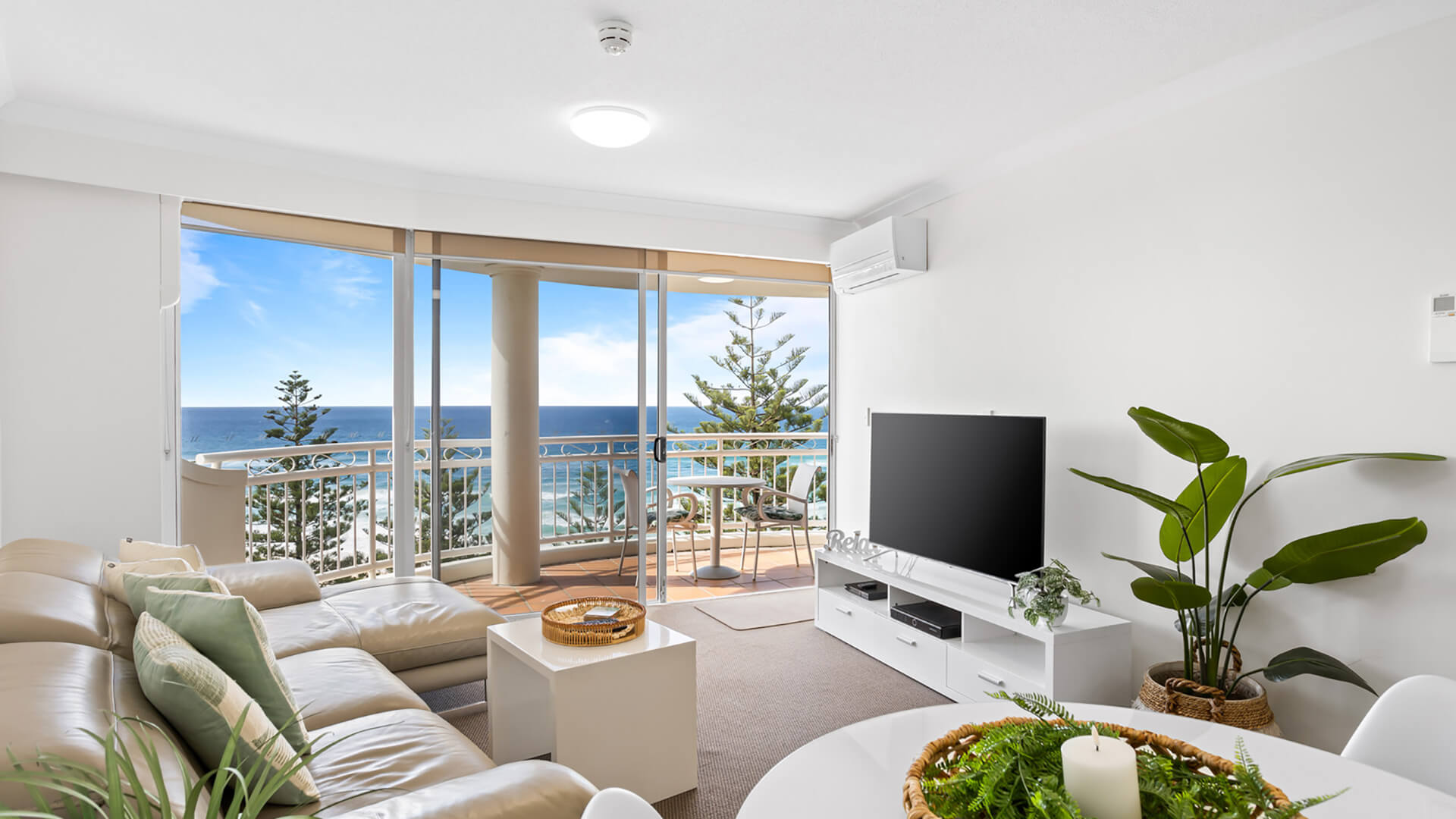 Open-plan living and dining area featuring a leather lounge, flat-screen TV, and balcony with sweeping ocean views.