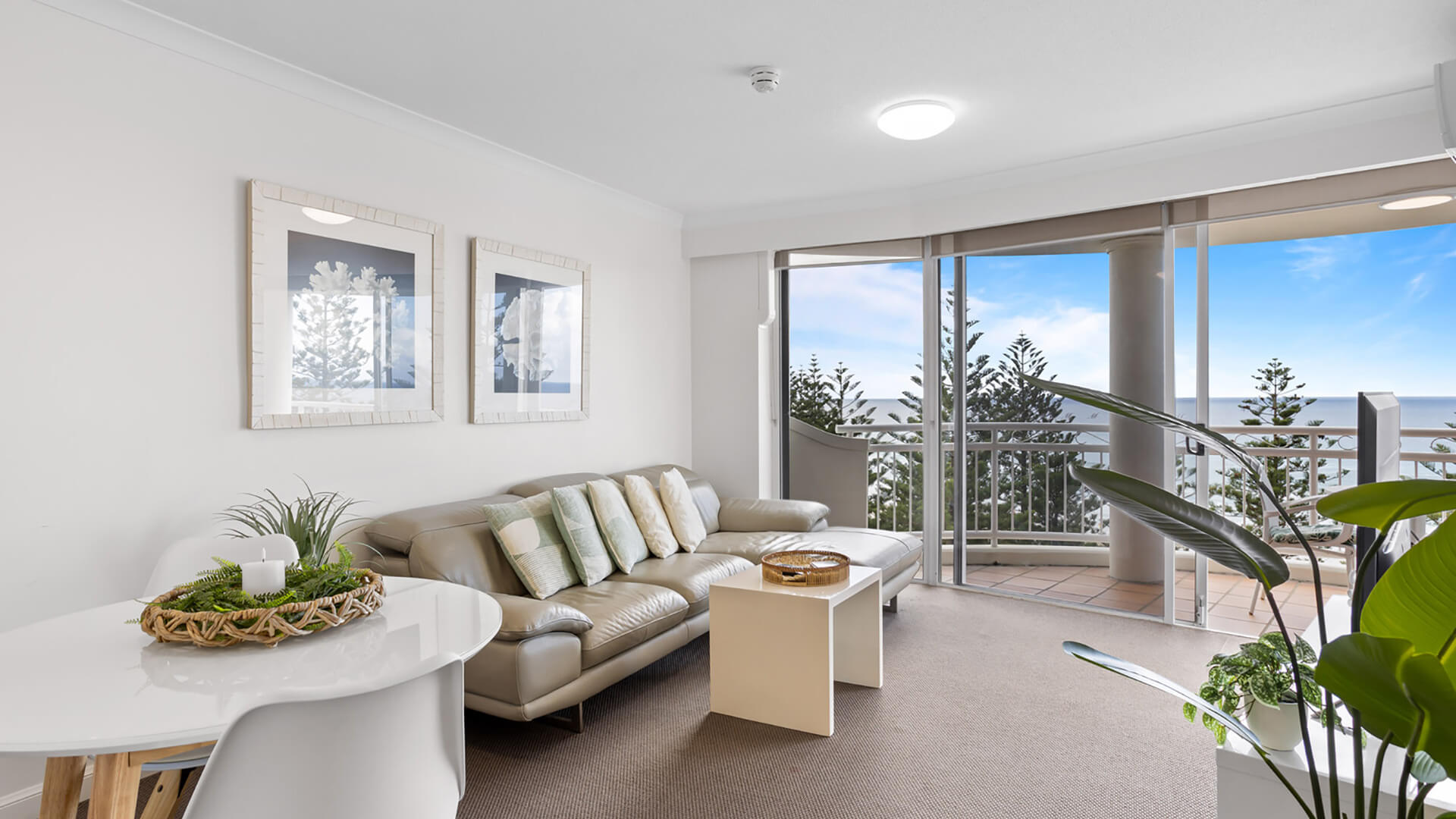 Bright living and dining area with coastal decor, leather sofa, and private balcony overlooking the ocean.