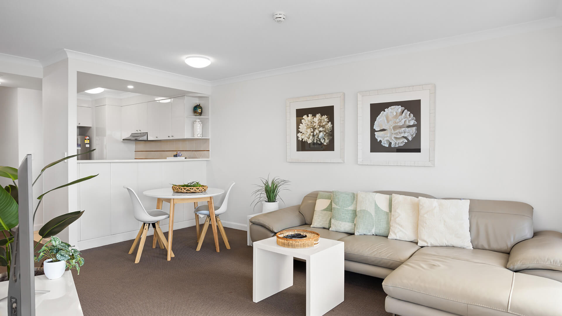 Open-plan living and dining area with a large leather sofa, coastal artwork, and modern kitchenette.