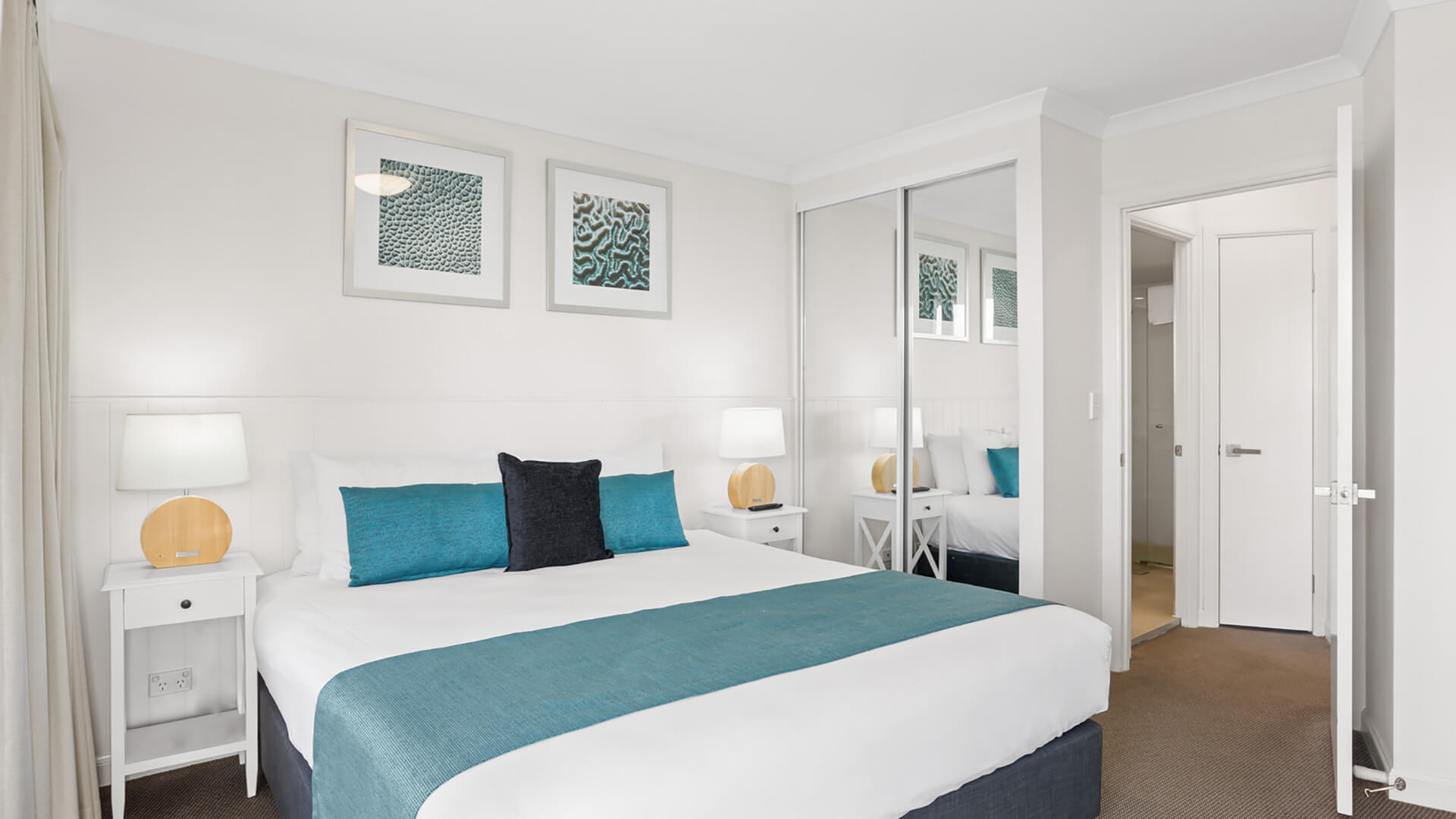King bedroom with mirrored wardrobe, bedside tables, and teal accents.