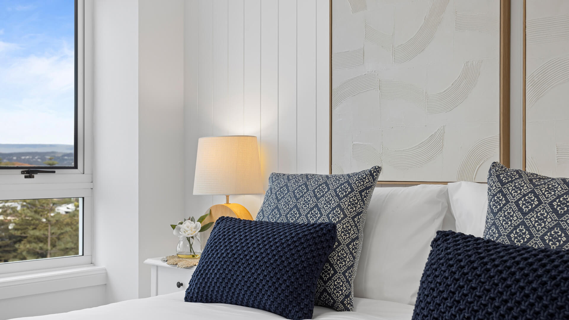 Close-up of the bedroom in the 3 Bedroom Superior Ocean View Apartment at ULTIQA Burleigh Mediterranean Resort, featuring blue accent pillows and soft lighting.