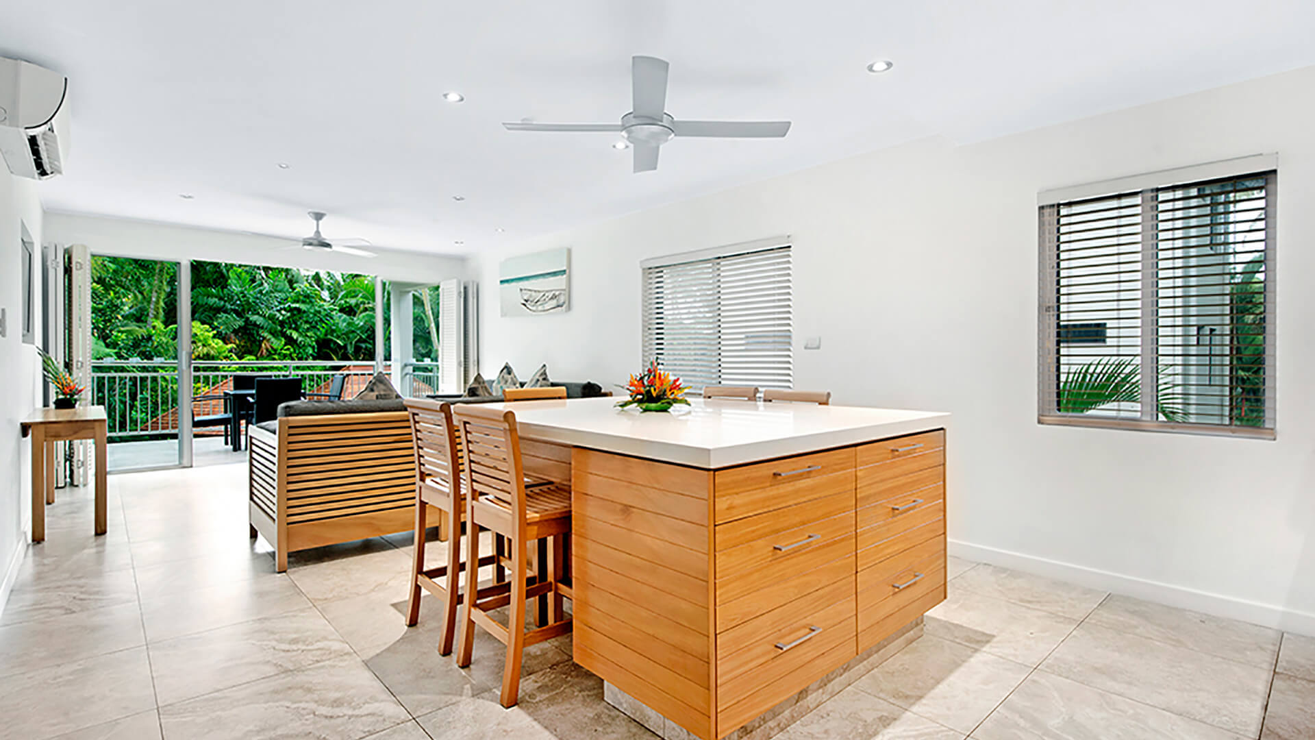 Open-plan living and kitchen area in 2 Bedroom Deluxe Apartment at ULTIQA Fiji with island bench, modern furnishings, and balcony overlooking tropical gardens.