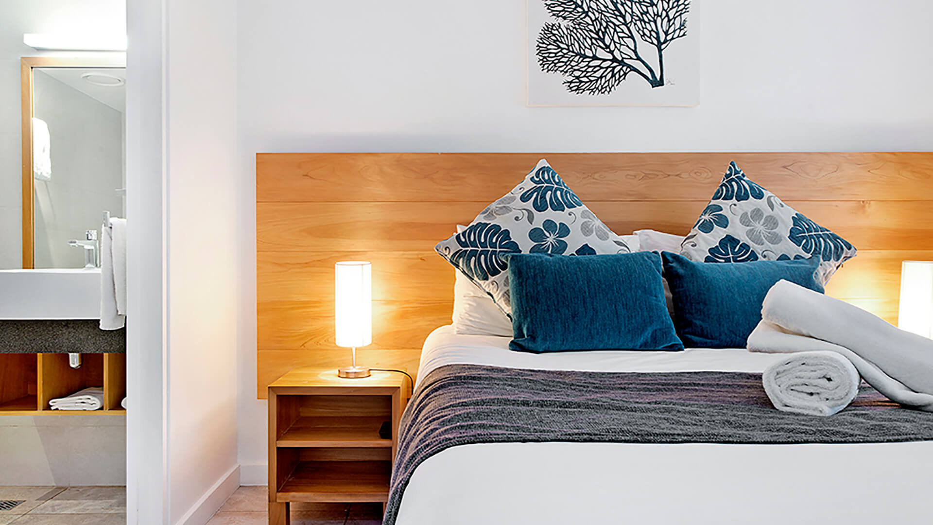 Cozy bedroom in 2 Bedroom Deluxe Apartment at ULTIQA Fiji with king bed, vibrant cushions, and ensuite bathroom access.