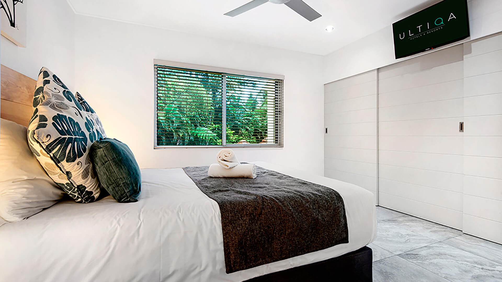 Bedroom in 2 Bedroom Deluxe Apartment at ULTIQA Fiji with tropical garden views, ceiling fan, and wall-mounted TV.