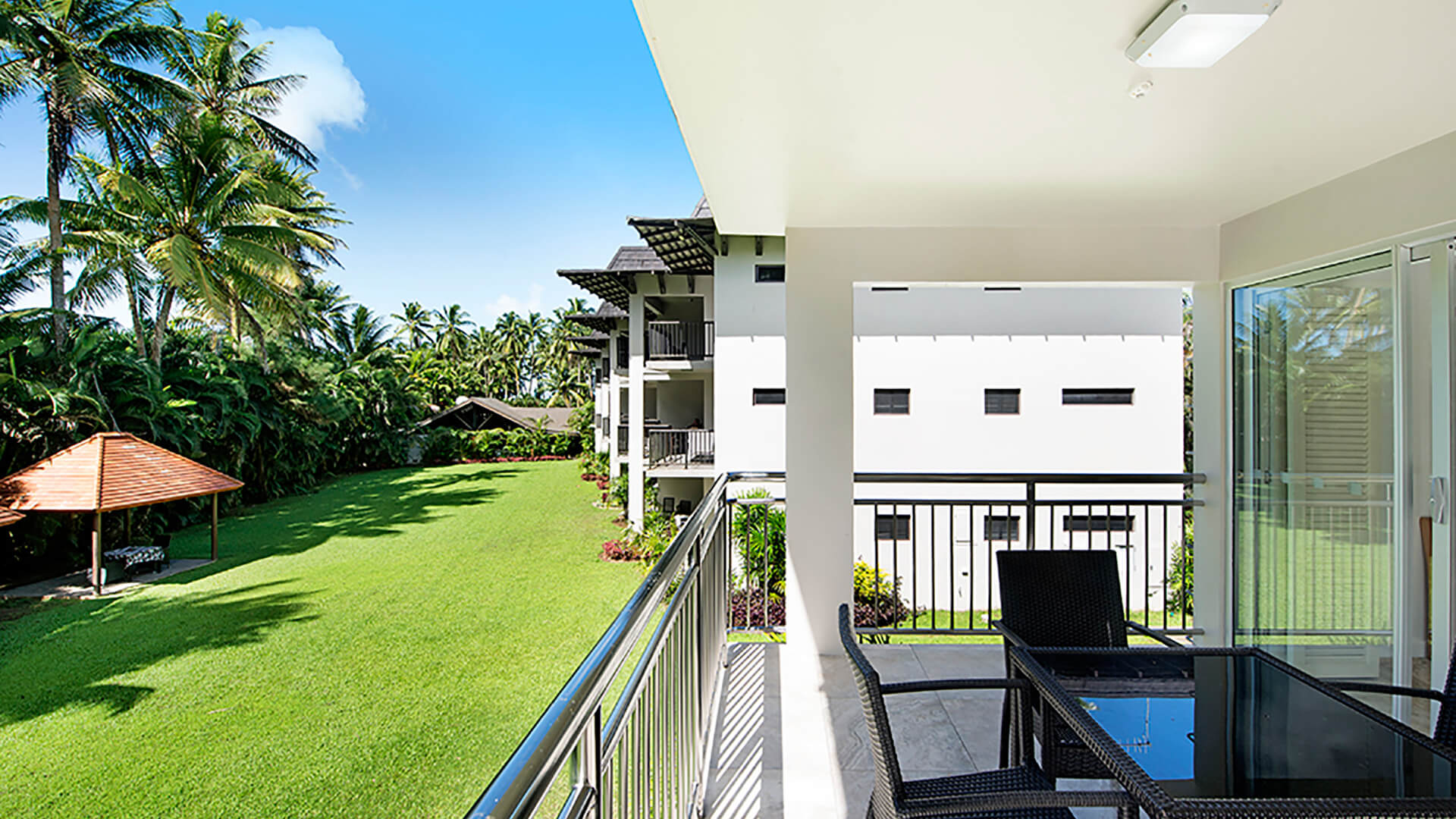 Balcony view from 2 Bedroom Deluxe Apartment at ULTIQA Fiji overlooking tropical gardens, lawn, and resort buildings.
