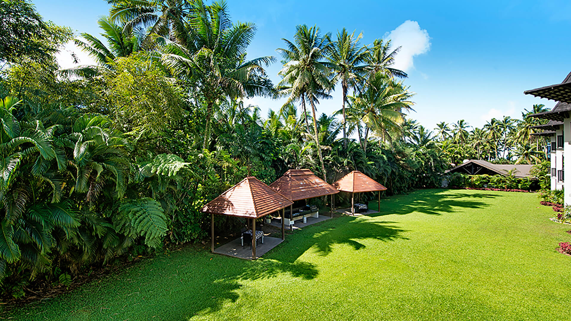 Tropical garden view at ULTIQA Fiji with lush palm trees, green lawn, and covered outdoor seating areas.