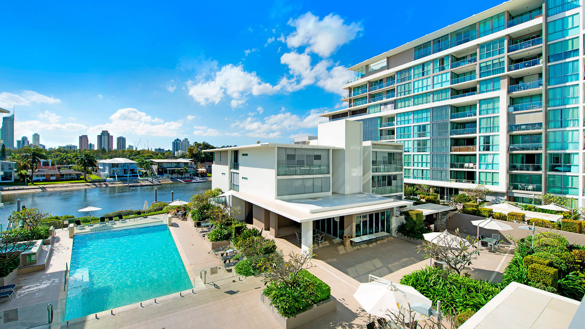 Pool and canal view from ULTIQA Freshwater Point Resort, featuring sun loungers, lush landscaping, and the Gold Coast skyline in the distance.