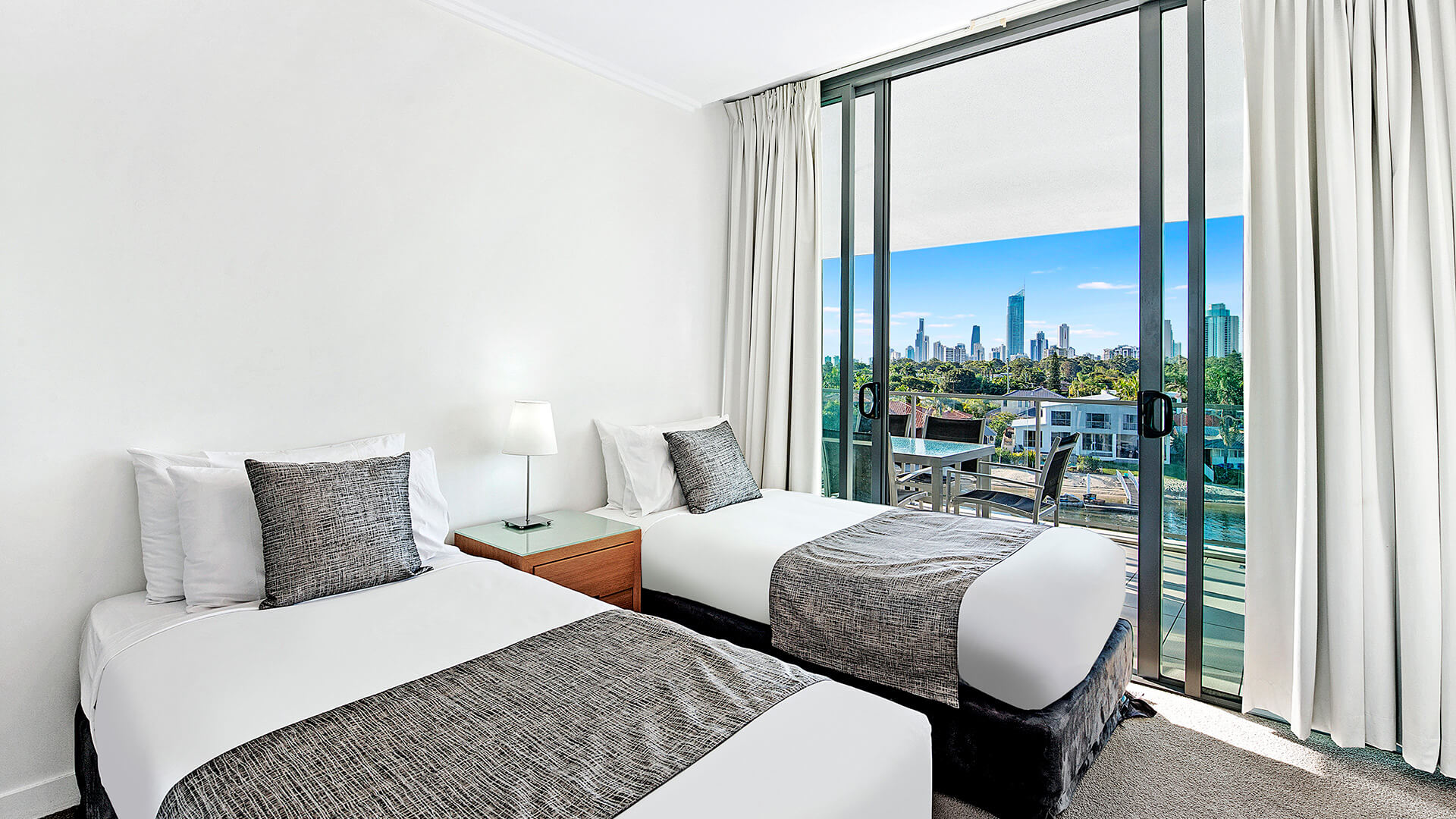 Second bedroom in the 2 Bedroom Apartment at ULTIQA Freshwater Point Resort, featuring two single beds and a private balcony with skyline views.