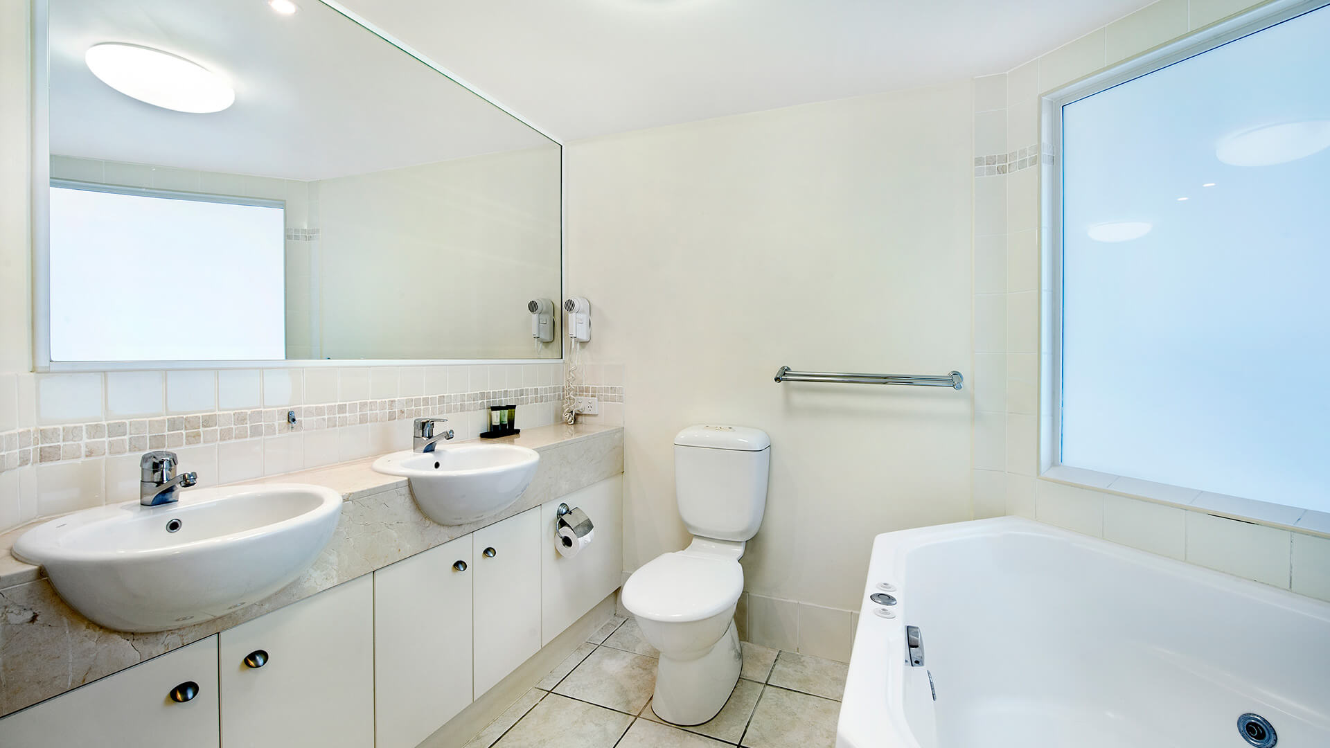 Bathroom with dual sinks, spa bath, and large mirror in Studio at ULTIQA Shearwater Resort.