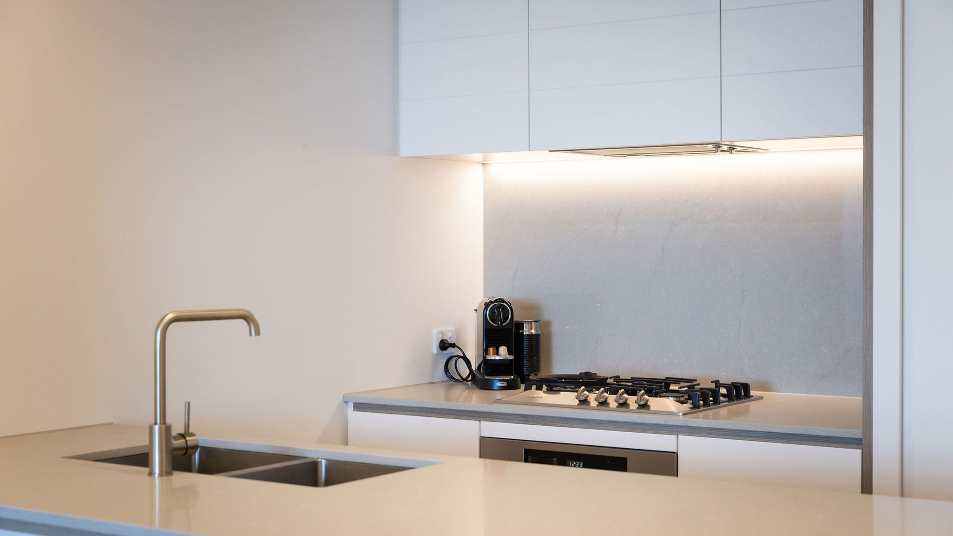 Close-up of modern kitchen with double sink, gas cooktop, and coffee machine in 1 Bedroom Ocean View Suite at ULTIQA Signature at Broadbeach.